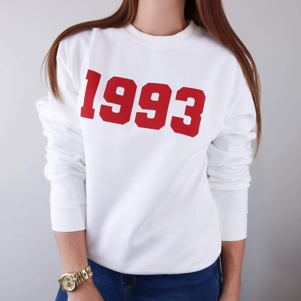 Woman wearing white hoodie with personalised year of 1993 in Red text also wearing blue jeans and gold watch. By Original Monkey Gifts.