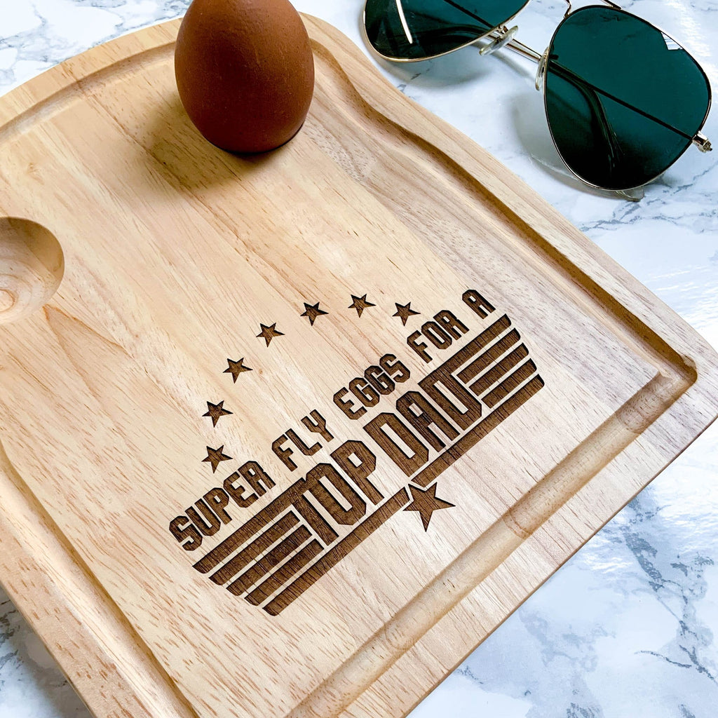 Egg board with message engraved that reads ' super fly eggs for a top dad' with stars by Original Monkey Gifts. Kitchen top with marble effect and sunglasses and also pictured.