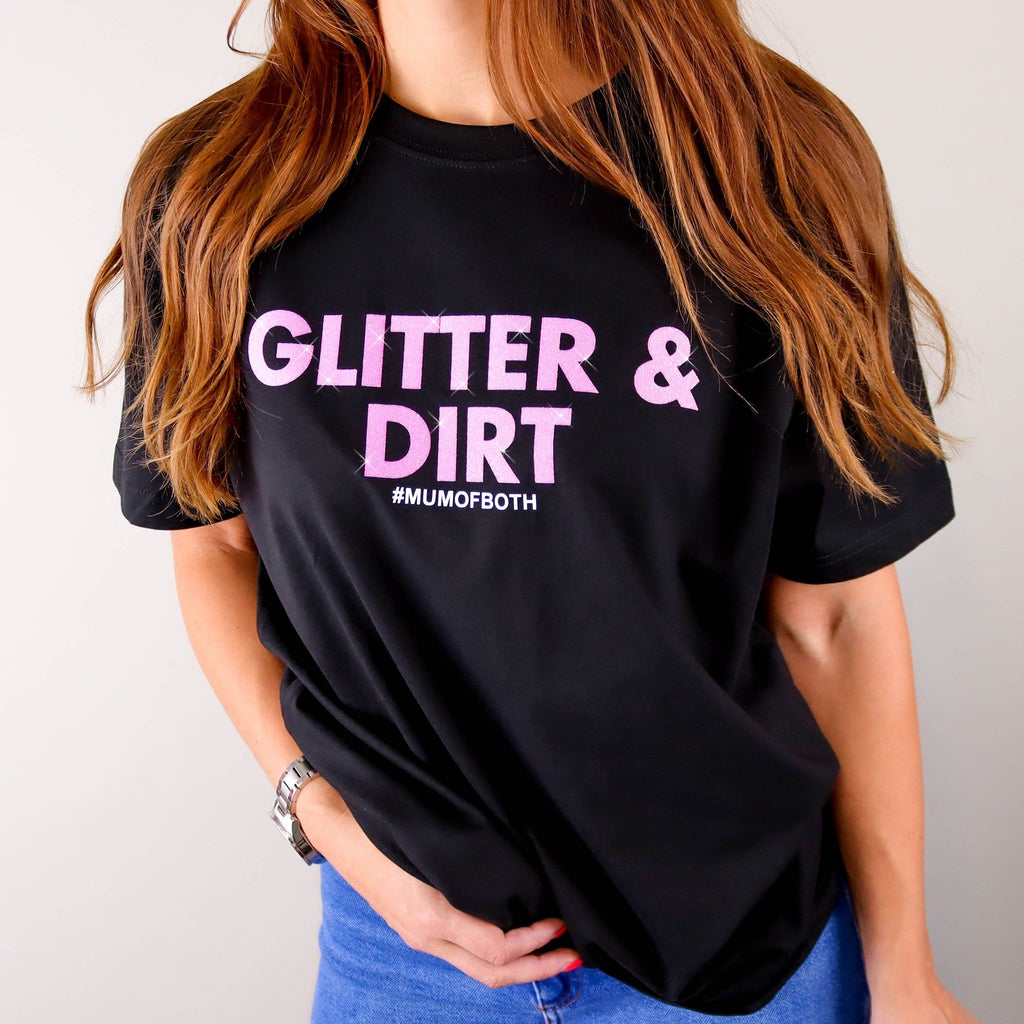 Woman wearing black T shirt with pink glittery text reading 'glitter and dirt #mum of both' by Original Monkey Gifts. Woman also wearing blue denim jeans.
