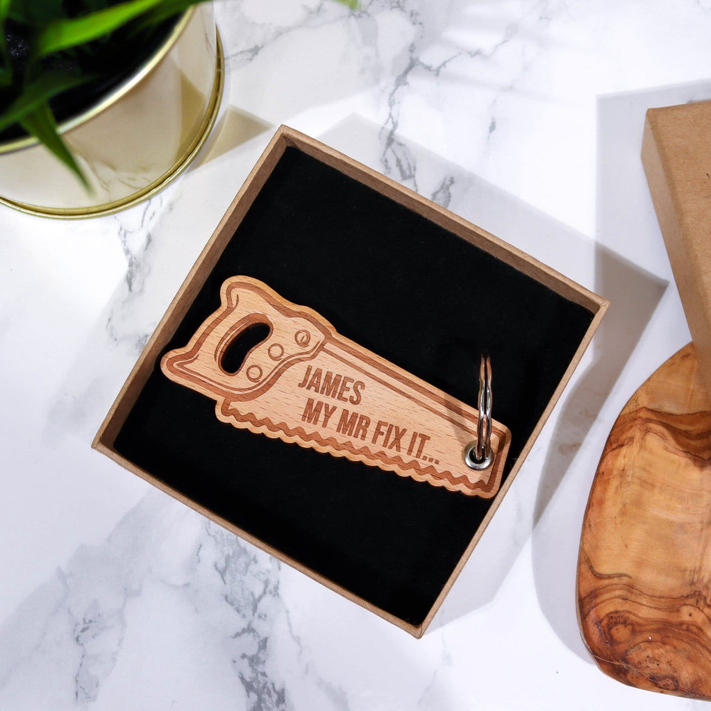 Man holding a saw shaped keyring that has a personalised message that reads 'James my mr mix it' by Original Monkey Gifts. A gift box and worktop are also pictured.