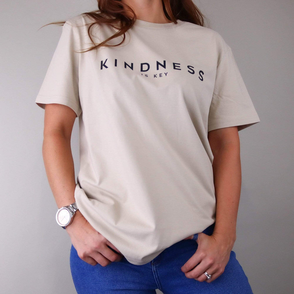 Woman wearing a nude t shirt with text that reads 'kindness is key' in black by Original Monkey Gifts. Woman also wears blue denim jeans, silver watch and white gold engagement and wedding rings.