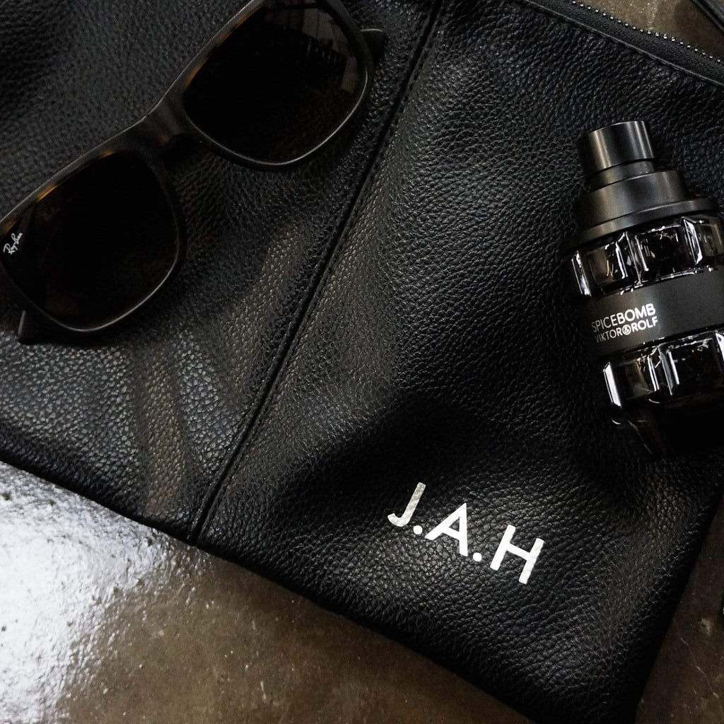 Black leather toiletries bag with personalised initials in silver by Original Monkey Gifts. Concrete worktop with toothbrush and mens hair products.