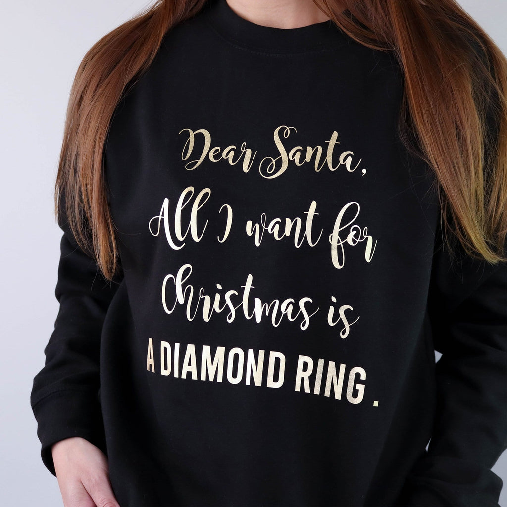Woman wearing black sweater with gold text reading 'All I want for Christmas is' which can be personalised by Original Monkey Gifts. Woman also wears blue denim jeans.