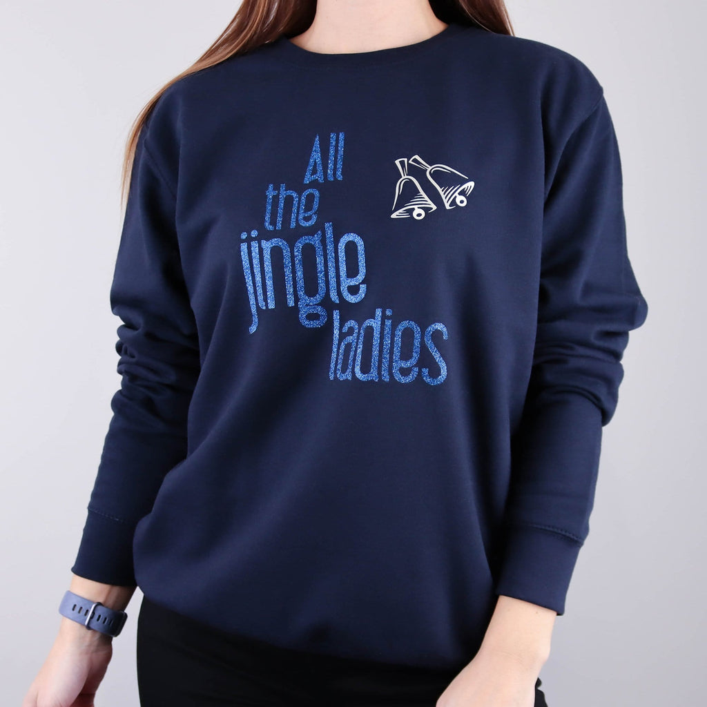 Woman wearing navy jumper with sparkly blue text that says 'all the jingle ladies' with silver bells made by Original Monkey. Woman also wears black denim jeans.