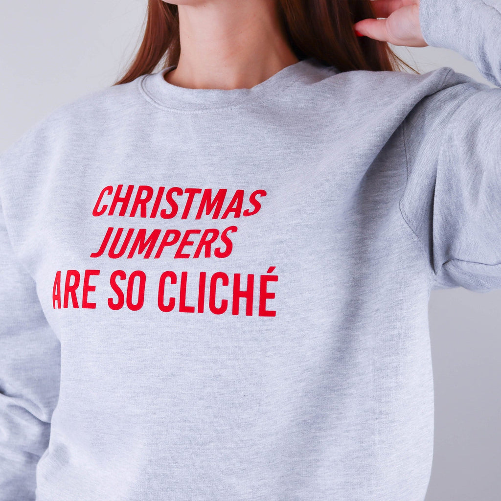 Woman wearing a grey sweater with red text that reads 'Christmas jumpers are so cliche' by Original Monkey Gifts.