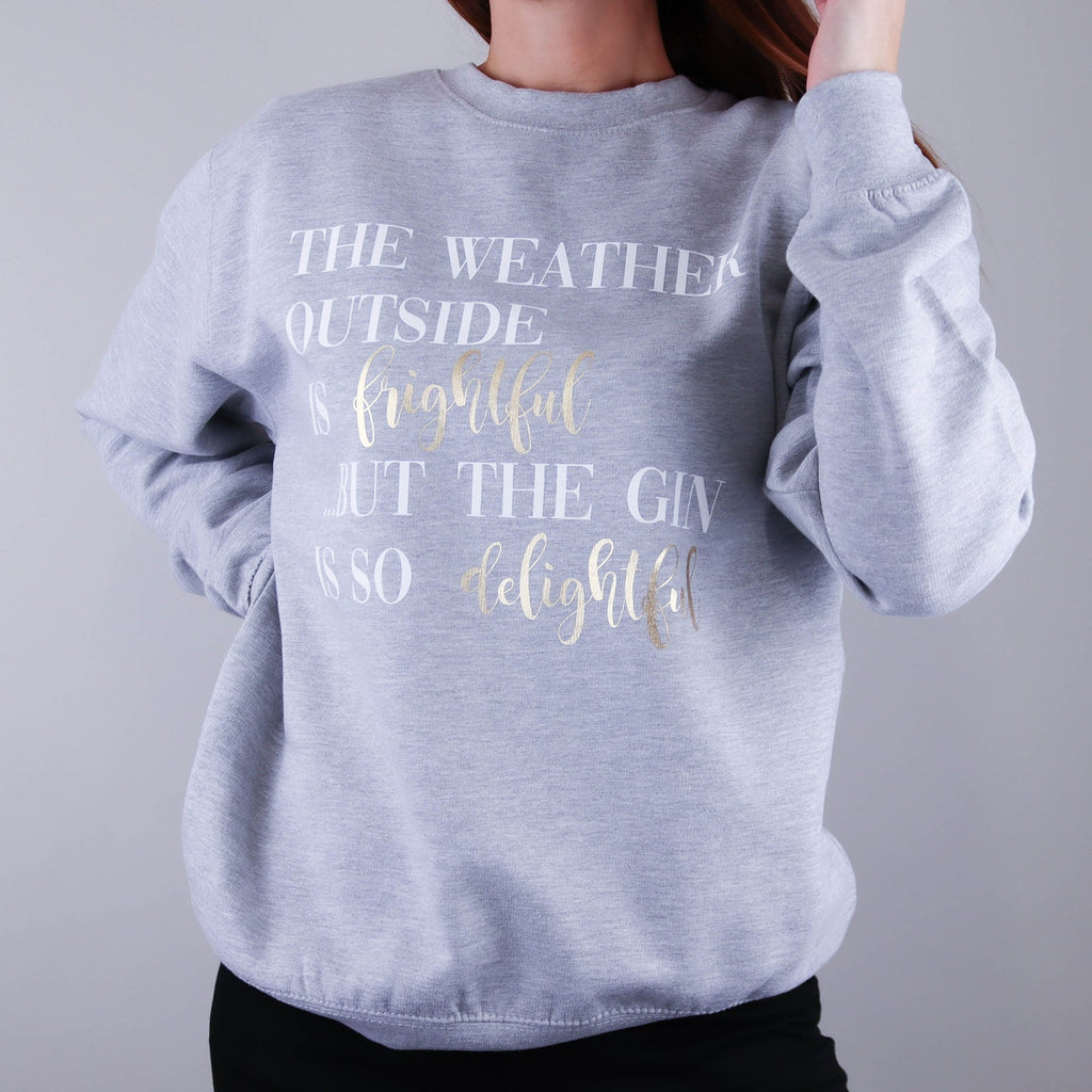 Woman wearing a grey jumper with text reading 'The weather outside is frightful but the gin is so delightful' by Original Monkey Gifts. Woman also wears black denim jeans.