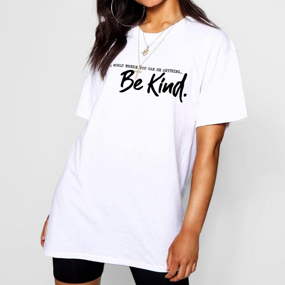Woman wearing a white t shirt with black text that reads 'in a world where you can be anything.. be kind' by Original Monkey Gifts. Woman also wears black leggings and gold necklace.