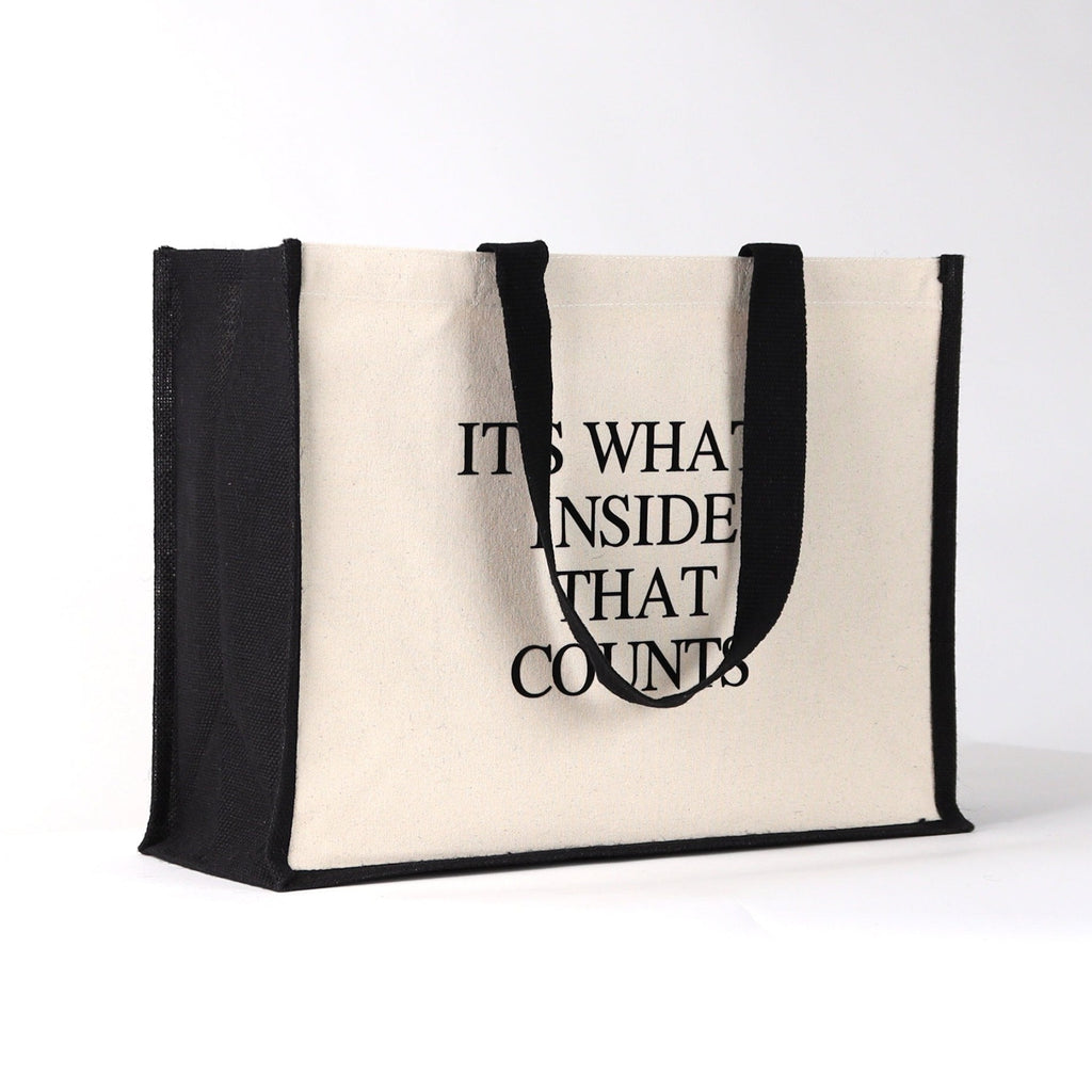 a black and natural tote bag with black wording saying "it's what's in side that counts" a great quality bag for everytday use, with a fashinable look to it