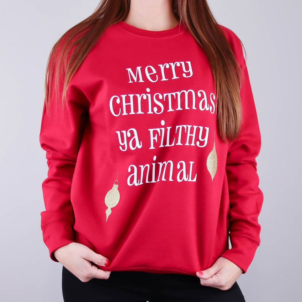 Woman wearing a red jumper with text the reads 'merry christmas ya filthy animal' from Home Alone 2 and gold baubles by Original Monkey Gifts.