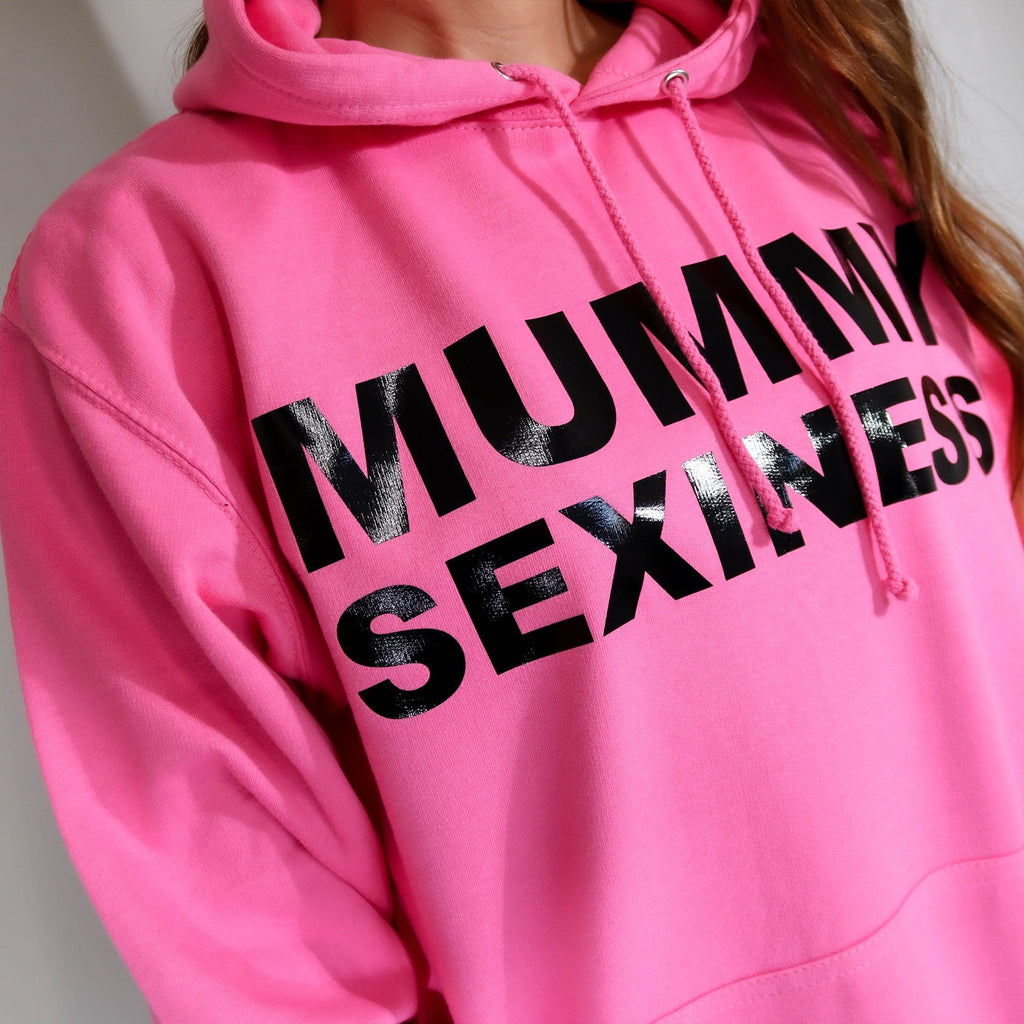 Woman wearing pink hoodie with text that says Mummy sexiness paired with blue denim shorts by Original Monkey Gifts