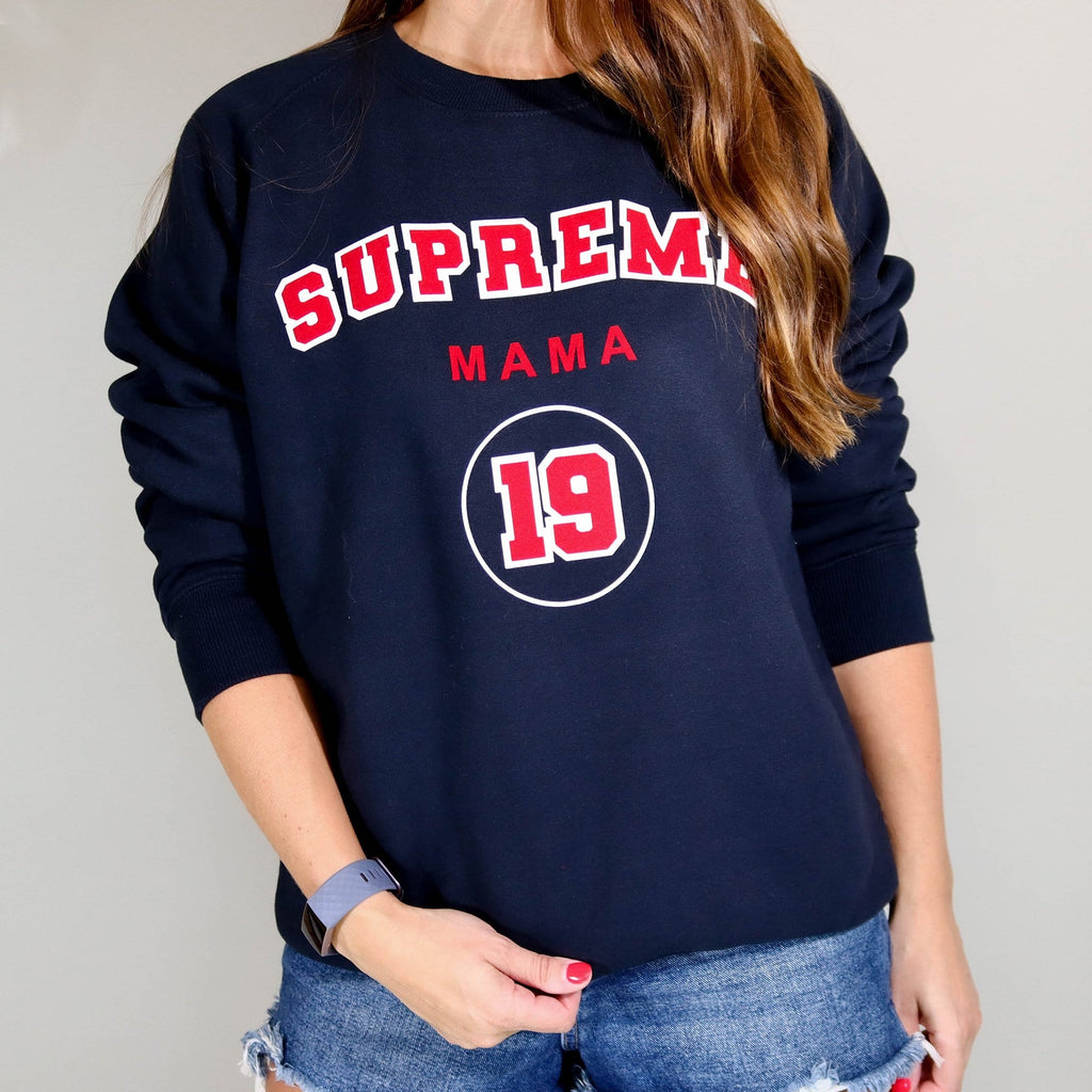 Woman wearing navy blue sweater with personalised Supreme Mama 19 in Red and white and is worn with blue denim shorts. By Original Monkey Gifts.