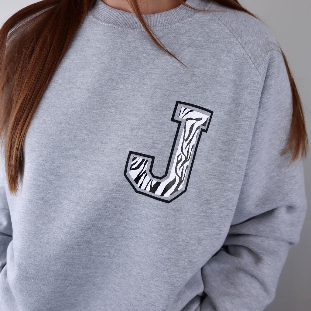Woman wearing a grey raglan sweater with a zebra print J initial on the front, paired with blue denim jeans. Made by Original Monkey Gifts