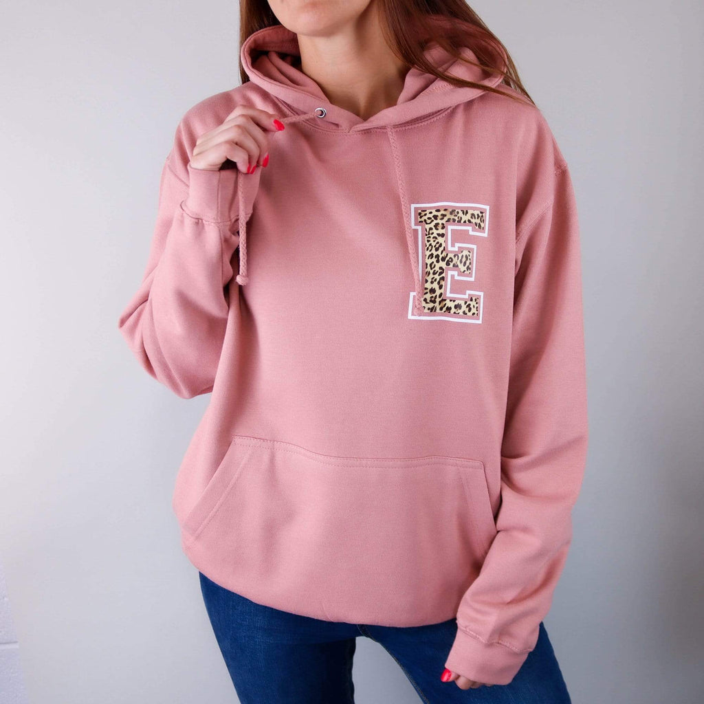 Woman wearing dusty pink hoodie with personalised letter E in Animal print text paired with blue denim jeans. By Original Monkey Gifts.