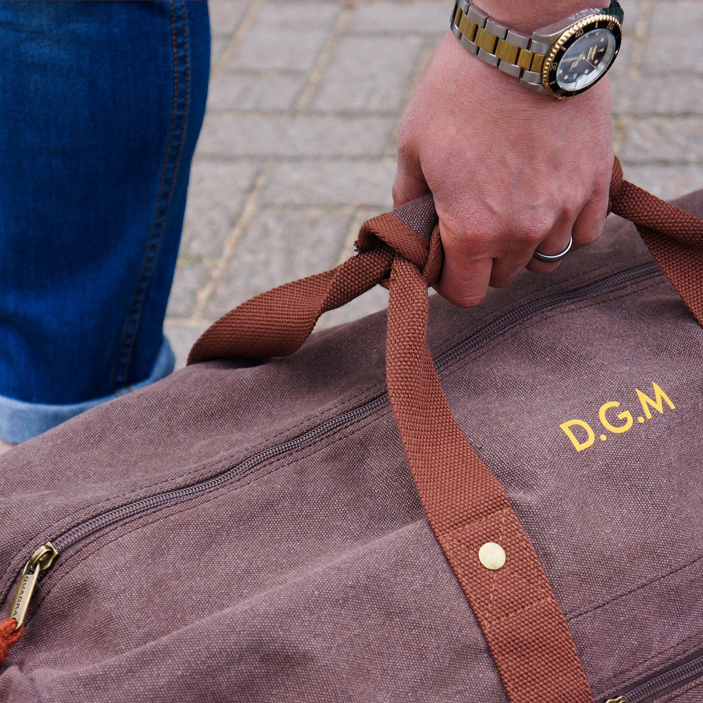 Man holding a canvas overnight bag in brown with personalised initial details in orange by Original Monkey Gifts.
