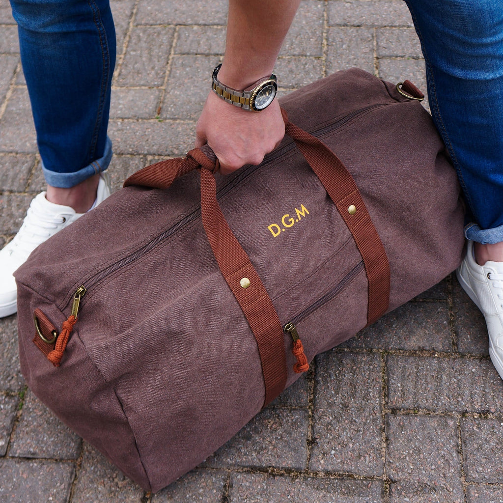 Man holding a canvas overnight bag in brown with personalised initial details in orange by Original Monkey Gifts.