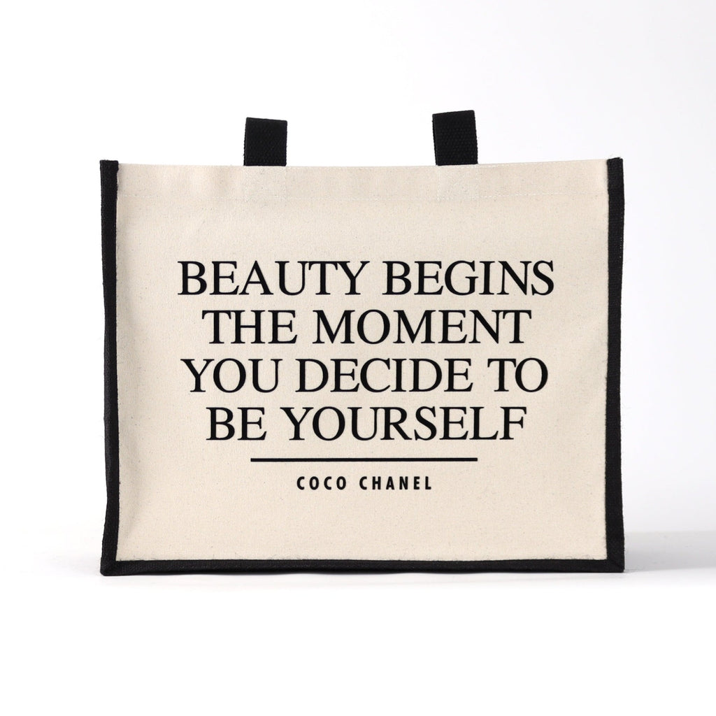 a black and natural tote bag with a fahion designer quote on it saying "beauty begins the moment you decide to be yourself"