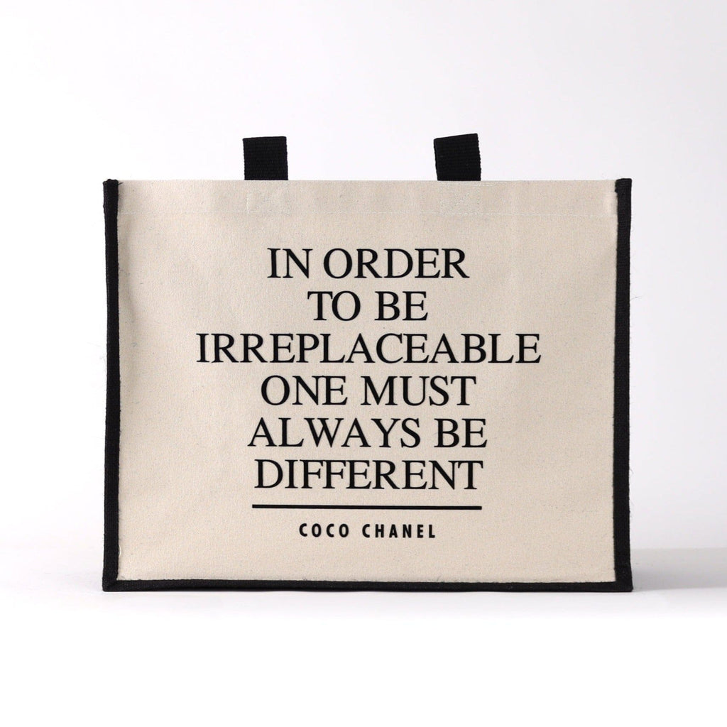 a black and natural tote bag with a famous qoute on it from a fashion designer " in order to be irreplaceable one must always be different"