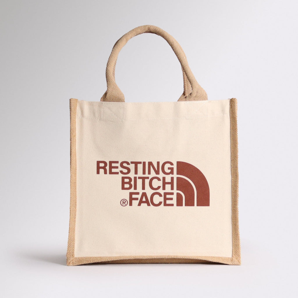 a natural coloured tote bag with a design on the front in a brown colour saying resting bitch face