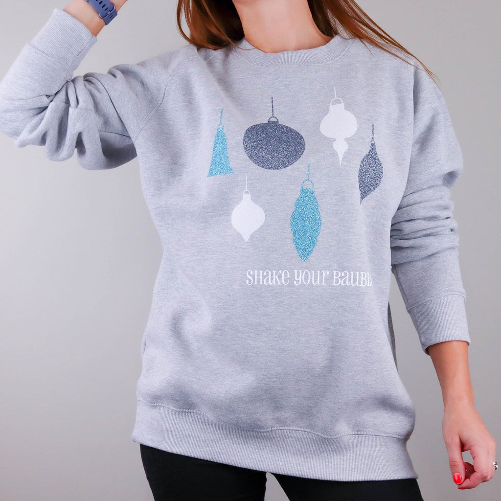 Woman wearing a grey sweater with sparkly bauble design with text that says 'shake your baubles' by Original Monkey.